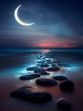 A group of rocks on a beach, illuminated by moonlight and set against the tranquil ocean. A pathway and small steps lead down to the shoreline, creating a sense of depth and perspective.