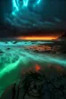 a large body of water under storm clouds with a bioluminescent effect, on a rocky coast with a teal-colored hue and multi-toned green and red lighting
